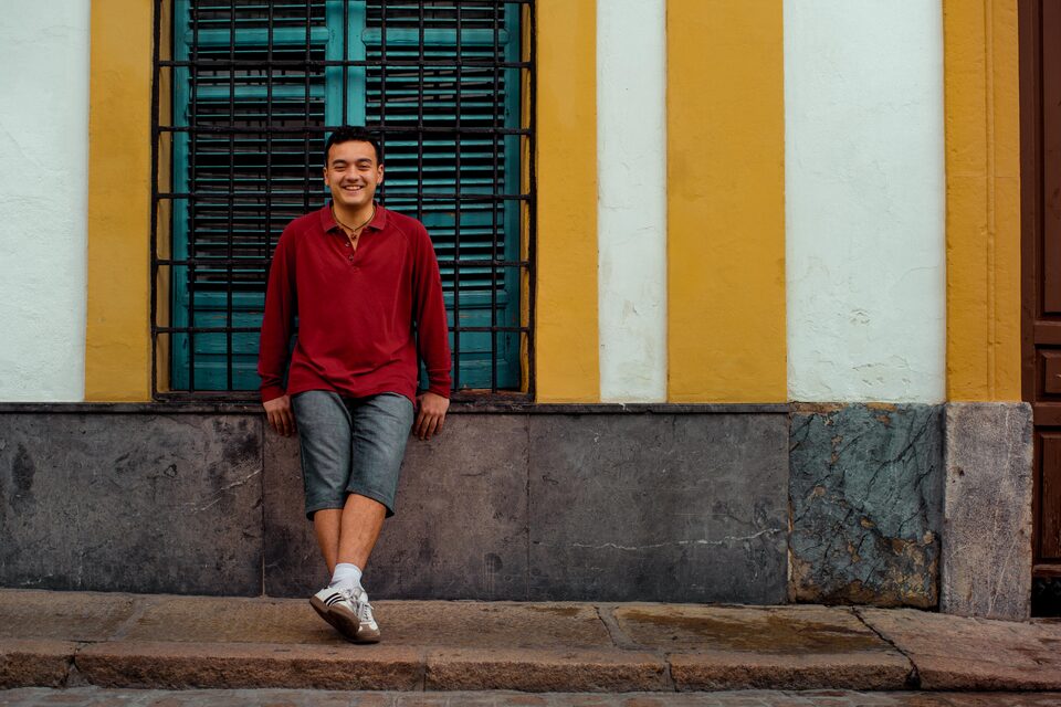 David sentado en el zócalo de una fachada de rayas amarillas, con una reja verde detrás